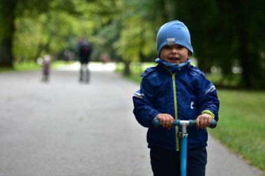 Orman yolunda scooter süren mutlu bir çocuk. Çocuk aktif açık hava oyunlarını, denge eğitimini ve ağaçlarla çevrili sağlıklı yaşam tarzını ve huzurlu doğal hayatı seviyor..