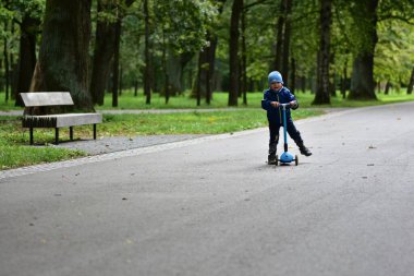 Orman yolunda scooter süren mutlu bir çocuk. Çocuk aktif açık hava oyunlarını, denge eğitimini ve ağaçlarla çevrili sağlıklı yaşam tarzını ve huzurlu doğal hayatı seviyor..