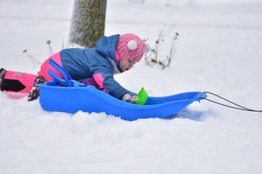 Bebek plastik kızağın üzerinde uzanıyor ve renkli oyuncak bardaklarla karla oynuyor. Tatlı çocuk kış eğlencesini, kar aktivitelerini, çocukluk anılarını ve mevsimsel yaşam tarzını seviyor..