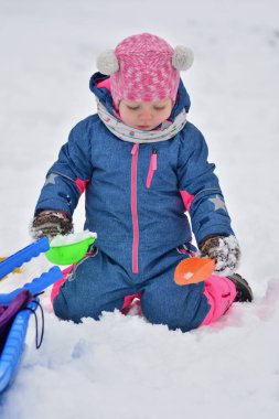 Bebek karda diz çöküp kış boyunca renkli plastik bardaklarla oynuyor. Karlı havanın, yaratıcı oyunların ve çocukluk keşiflerinin tadını çıkaran ılık kar giysisi içindeki sevimli çocuk..
