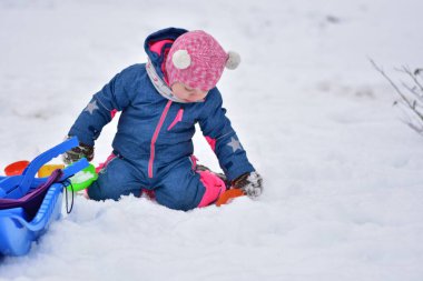 Taze karda renkli plastik oyuncaklarla oynayan küçük bir kız. Sıcak kış kıyafetleri içinde sevimli bir çocuk soğuk bir günde açık havada kış aktivitesi, duyusal oyun ve ilk kar deneyimiyle eğleniyor..