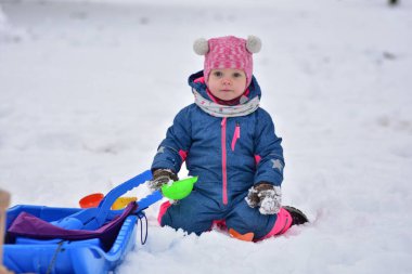 Taze karda renkli plastik oyuncaklarla oynayan küçük bir kız. Sıcak kış kıyafetleri içinde sevimli bir çocuk soğuk bir günde açık havada kış aktivitesi, duyusal oyun ve ilk kar deneyimiyle eğleniyor..