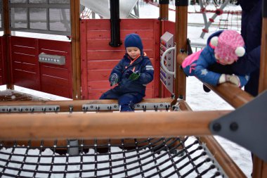 İki çocuk ve babam kışın modern bir oyun parkı köprüsünde birlikte oynuyorlar. Sıcak renkli kar giysileri giyen çocuklar karlı bir günde denge ve koordinasyonu keşfettiler..