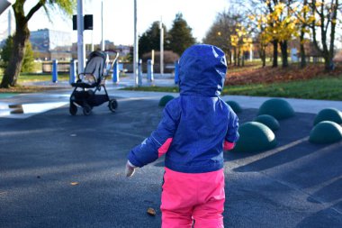 Sonbahar parkında modern oyun parkında yürüyen bir çocuk. Güneşli bir sonbahar gününde çocuk ceketini ve pantolonunu giyip açık hava oyun alanını, çocukluğu ve keşif kavramını keşfediyor..