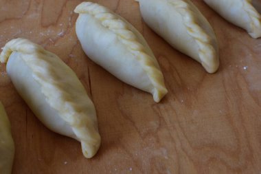 Tahta üzerinde geleneksel Karaim kibinai hamur işleri. Fırınlanmamış hamur köfteleri, Trakai, Litvanya 'da popüler, genellikle pierogi ile karşılaştırılır ve ev yemeği ya da şenlikli yemekler için yapılır..