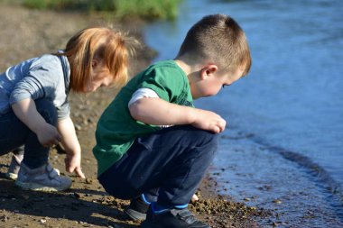 Genç bir oğlan ve kız nehir kenarında çömelmiş ıslak kuma ve küçük çakıl taşlarına dokunuyorlar. Doğayı keşfeden meraklı çocuklar sıcak güneş ışığında, huzurlu çocukluk maceralarını paylaşıyorlar..