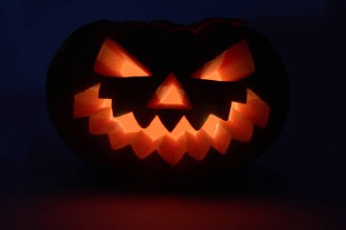 Işıldayan bir balkabağı kabağı, parlak bir balkabağı yüzüyle karanlık bir arka plana doğru aydınlatılır.