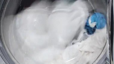 Çamaşır makinesinde çamaşır ve çamaşır yıkama, çamaşır makinesinde çamaşır yıkama, çamaşır makinesinde hareket halindeki kıyafetlerin yakın çekimi.