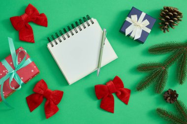 Noel kompozisyonu köknar dalları, not defteri, bir kalem ve yeşil arka planda bir hediye kutusu.