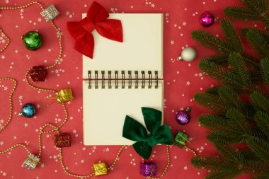 Ortadaki boş defteri aç. Noel ağacı dalları, tatil süslemeleri ve kırmızı arka plandaki hediyelerle çevrili.