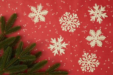 Beyaz parlak kar taneleri, kırmızı zemin üzerinde yeşil çam dalları ve yıldız ve noktalarla süslü Noel dairesi. Tatil dekorasyonu