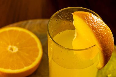 Bir bardak taze sıkılmış portakal suyu, yanında da cam kamış ve portakal dilimleri ve yanında da ahşap tepsi var..