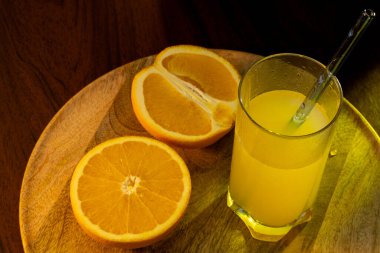 Bir bardak taze sıkılmış portakal suyu, yanında da cam kamış ve portakal dilimleri ve yanında da ahşap tepsi var..