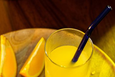 Bir bardak taze sıkılmış portakal suyu, yanında da cam kamış ve portakal dilimleri ve yanında da ahşap tepsi var..