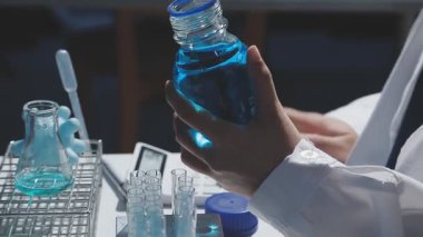 Tıbbi ya da bilimsel araştırmacı ya da insan doktoru laboratuarda bir test tüpü dolusu temiz çözeltiye bakıyor.