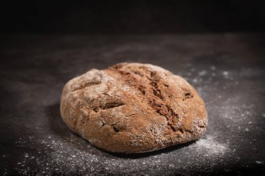 Kırsal kepekli ceviz ekmeği un kaplı, koyu levha yüzeyinde, kabuklu ev yapımı somun ekmeği yukarıdan aşağıya doğru açılı, taze kırıntılar ve doku görünür, içten bir zanaatkar sunumu.