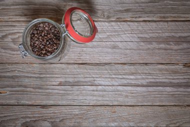 Kavrulmuş kahve çekirdekleri açık cam kavanozda, beyazlatılmış ahşap masada, sol üstteki konumda, düz konumda, çerçevenin geri kalanı mesaj veya tasarım için bolca boş alan bırakıyor..
