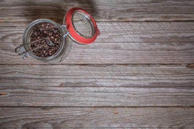 Kavrulmuş kahve çekirdekleri ile dolu açık cam kavanozun içindeki metal ölçüm kaşığı aşınmış ahşap masa, sol üst konum, düz konum çerçevenin geri kalanı yazı veya tasarım için bolca boş alan bırakıyor..