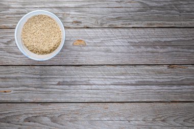 El yapımı seramik kasede pişirilmemiş pirinç, aşınmış ahşap yüzeyde yukarıdan çekilmiş. Resim, doğal stüdyo bileşimindeki basit tahıl bileşenini belgeliyor.