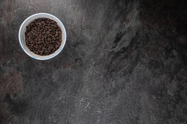 Stüdyonun düz yüzeyinde koyu renk tahta üzerine yerleştirilmiş kavrulmuş kahve çekirdekleri ile dolu el yapımı seramik kâse. Çerçevenin geri kalanı metin veya tasarım için bir sürü boş alan bırakır.