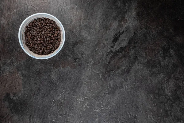 Stüdyonun düz yüzeyinde koyu renk tahta üzerine yerleştirilmiş kavrulmuş kahve çekirdekleri ile dolu el yapımı seramik kâse. Çerçevenin geri kalanı metin veya tasarım için bir sürü boş alan bırakır.