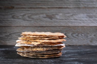 Stacked round sourdough crispbread on slate surface, side view, blurred wooden wall, homemade Scandinavian knckebrot