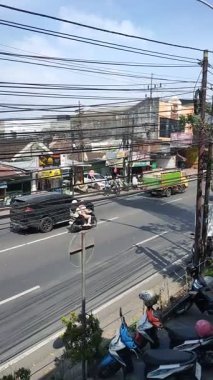 Bir teslimat kamyonu, motosikletler ve parlak bir gökyüzü altında işlek bir şehir ortamında gezinen arabalarla dolu bir sokak manzarası. Malang, Doğu Java, Endonezya. 3 Ekim 2025.