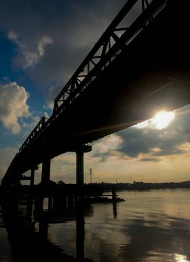 Kapuas Köprüsü 'nün alçak açılı bir görüntüsü. Güneş, geniş nehrin üzerinden yükselirken parlak mavi bulutsuz gökyüzünün altındaki ışığı yansıtıyor.
