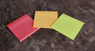 Kahverengi bir yüzeye üç canlı yapışkan nota yerleştirilir..