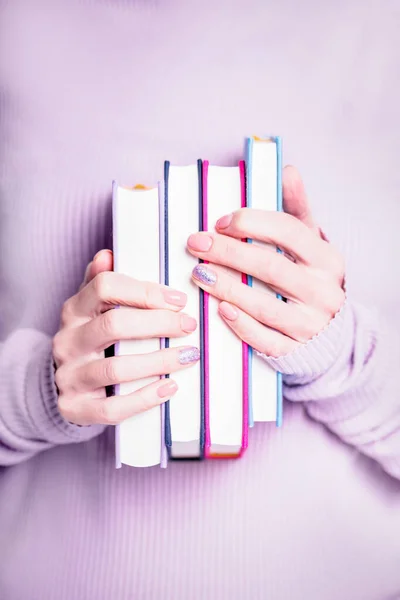 紫色の背景に4冊の本を持つ手 — ストック写真