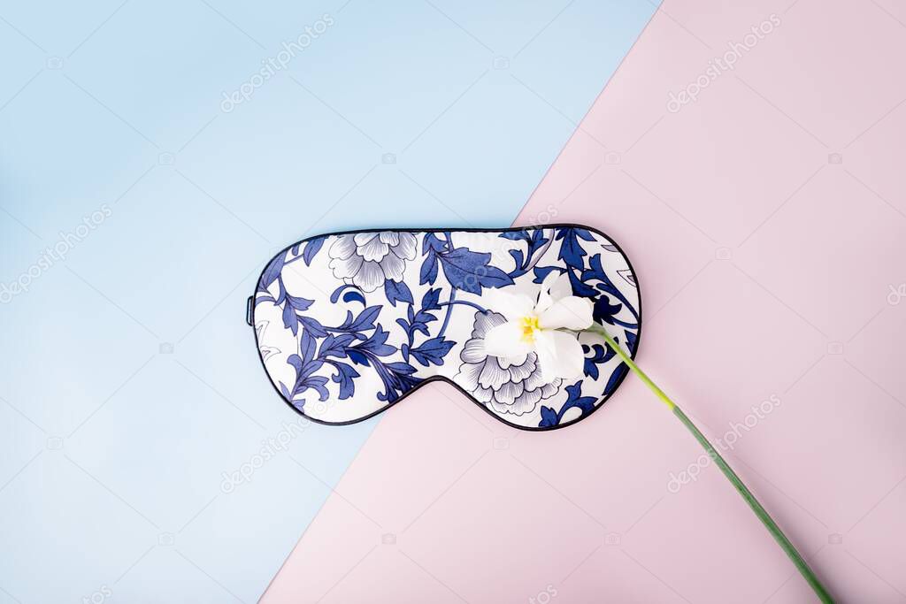 Beautiful silk sleep mask for eyes with flowers pattern and white daffodil or narcissus flower on a geometric pink blue background
