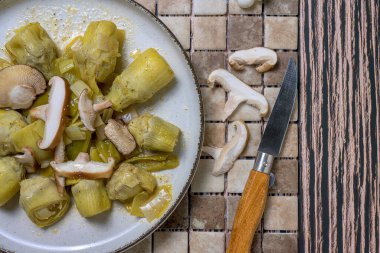 Köy arka planında servis edilen taze mantarlı pişirilmiş enginar tabağı, sağlıklı yemek ve sonbahar mutfağı için mükemmel.