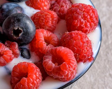 Bir kase sütte taze ahududu ve yabanmersini yakın plan (ya da bitki bazlı süt). Sağlıklı kahvaltı, diyet, süper yemek ve vegan yaşam tarzı kavramları için idealdir.