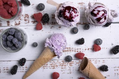 Waffle külahında bir kepçe yaban mersinli dondurma, taze ahududu ve beyaz ahşap üzerinde böğürtlen.