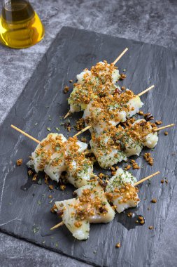 Kızarmış sarımsak ve taze maydanozla kaplanmış morina balığı şişleri.