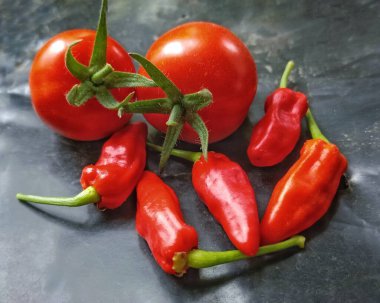 Parlak kırmızı biberli, sarmaşıklı, olgun kırmızı domatesler etrafa saçılmış. Gıda, yemek, pazar ve aşçılık projeleri için ideal.