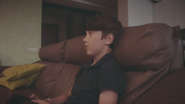 Мальчик играет в видеоигры на консоли на диване дома — стоковое видео