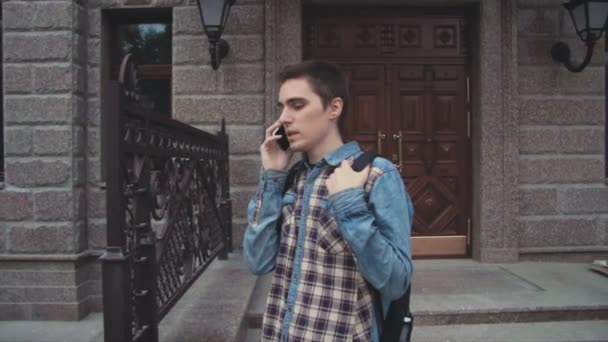 Joven hombre contemporáneo caminando por la calle y hablando por teléfono — Vídeos de Stock