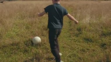 Küçük çocuk futbol alanında oynuyor. Çayır topuyla aracılığıyla çalışan çocuk. Kırsal ve orman