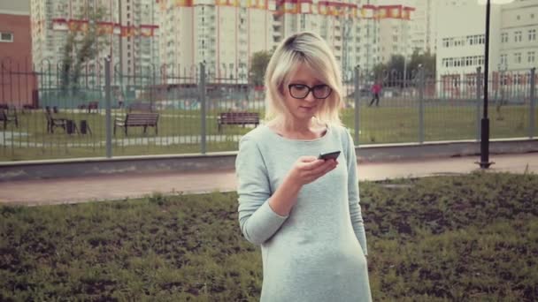 Mujer joven feliz de pie en el área del parque entre los edificios utilizando su teléfono inteligente mensajes de texto — Vídeo de stock