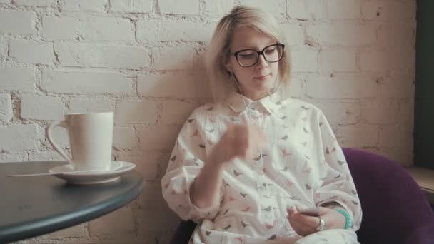 Feliz joven hermosa mujer bebiendo café en el café y escuchando música en el iPod — Vídeo de stock