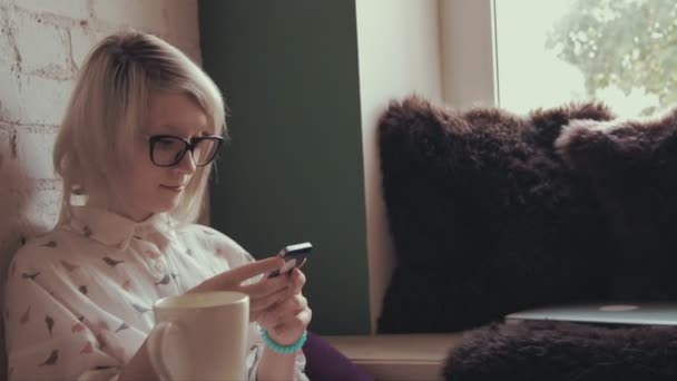 Wanita cantik yang bahagia minum kopi di kafe dan SMS di telepon pintarnya — Stok Video