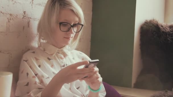 Feliz joven hermosa mujer bebiendo café en el café y mensajes de texto en su teléfono inteligente — Vídeos de Stock