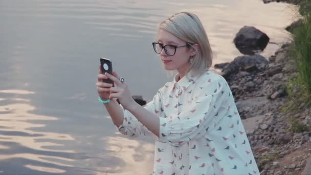 Joven hermosa mujer tomando fotos con su teléfono inteligente en el parque de la ciudad cerca del lago — Vídeos de Stock