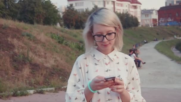 Fiatal gyönyörű nő séta a parkban, a tónál, használ neki smartphone, textil barátai, internetes böngészés, görgetés app — Stock videók