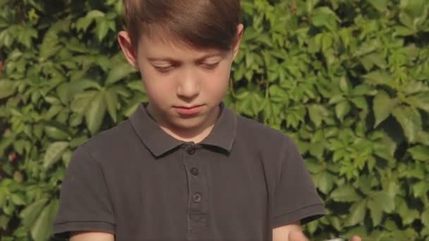 Niño jugando juegos en su tableta de pantalla táctil al aire libre en frente de la casa cubierta de vegetación — Vídeo de stock