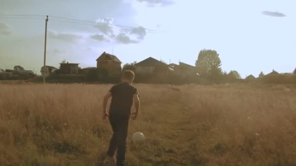 Un niño jugando al fútbol en el campo. Niño corriendo por el prado con una pelota. Campo y bosque — Vídeo de stock