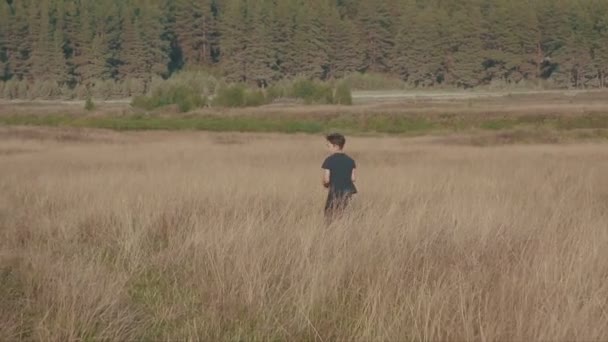 Un niño jugando al fútbol en el campo. Niño corriendo por el prado con una pelota. Campo y bosque — Vídeo de stock