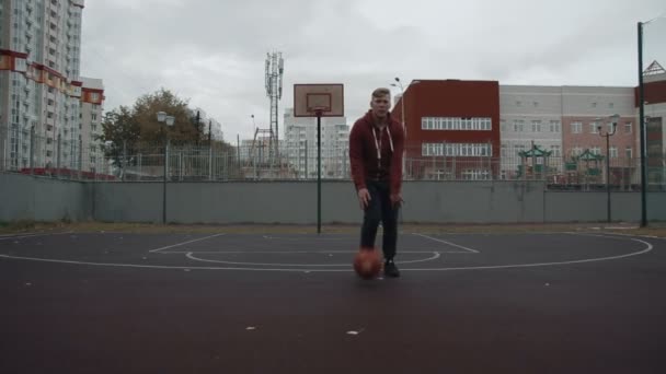 Молодий чоловік грає в баскетбол на відкритому повітрі на дворі — стокове відео