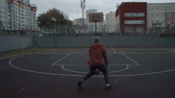 Молодой человек играет в баскетбол на открытом воздухе на площадке — стоковое видео